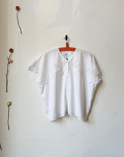 White blouse with scalloped lace trim hanging on the wall